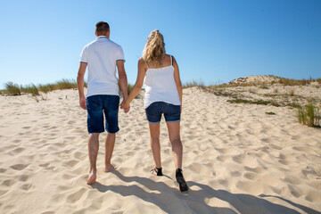 Couple in love young walk holding hands on the beach sand dune in summer holidays