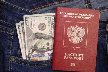 Fototapeta premium A stack of American hundred dollar bills in a pocket of blue jeans and an international passport of the Russian Federation. Money in your pocket, cash. Travel concept.