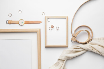 Stylish wristwatch, blank photo frame and rings on light background