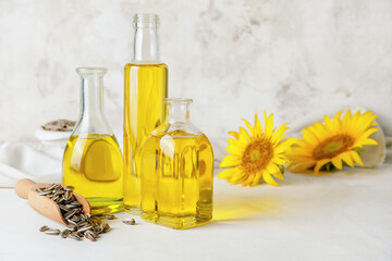 Bottles of oil, scoop with seeds and sunflowers on light background