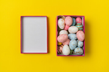 Top view of rectangular box with Easter eggs on yellow background. Multicolored festive eggs