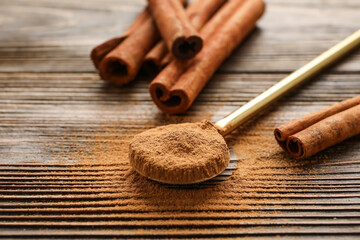 Cinnamon sticks and spoon with powder on wooden background