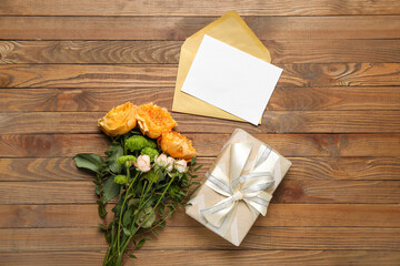 Bouquet of beautiful flowers, gift and blank card on wooden background