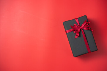 Black gift box with red bow on red background top view, Valentines day, Flat lay style with copy space.