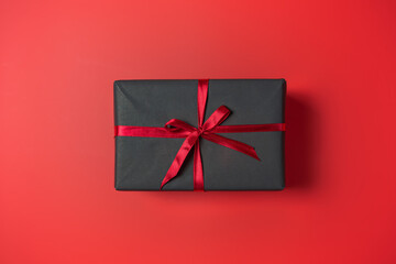 Black gift box with red bow on red background top view, Valentines day, Flat lay style with copy space.