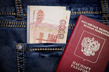 A stack of Russian five-thousandth and one thousand-ruble bills in a pocket of blue jeans and a Russian international passport. Money in pocket cash. Travel concept.