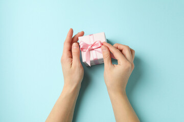 Female hands holding gift box with pink ribbon on blue background