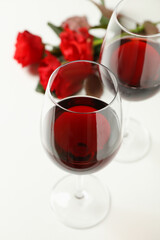 Red roses and glasses of wine on white background