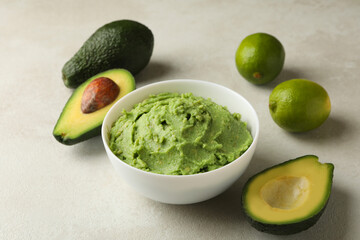 Bowl of guacamole, avocado and lime on white textured background, close up
