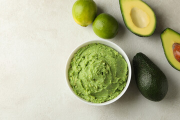 Bowl of guacamole, avocado and lime on white textured background, space for text