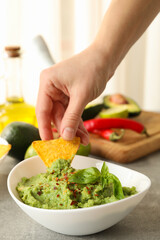 Female hand dips chips slice in guacamole