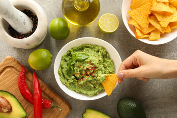 Female hand dips chips slice in guacamole, top view