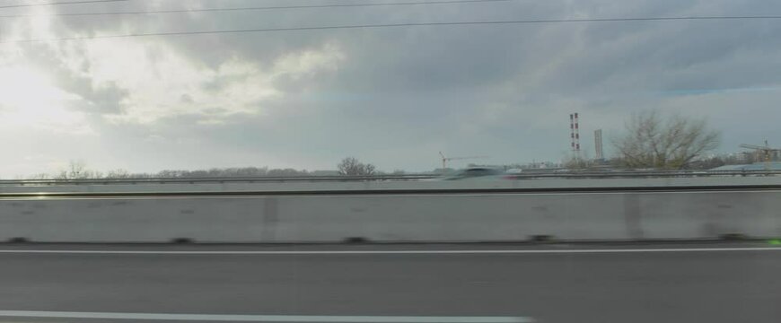 Side view through car window while driving on multiple lane road. Tall striped factory chimneys in distance. Car driver's point of view.