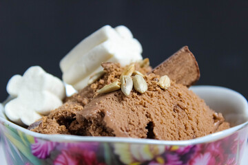 Chocolate ice cream in a bowl, decorated with marshmallows, seeds and chocolate chips.