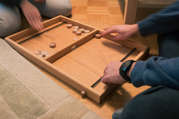 Wooden bard game where you shoot round wooden blocks through opening with help of an elastic band. Two players visible.