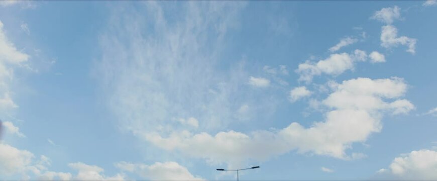 Blue sky with several white clouds. Camera tilted up to sky while driving in town. Car driver's point of view.
