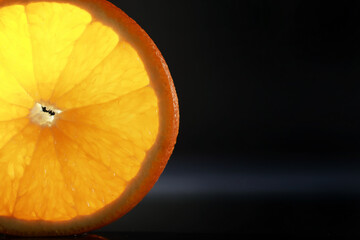 Composition with orange and grapefruit slices on a black background. A slice of orange with back light on a black background with water drops. Juicy orange on a table.