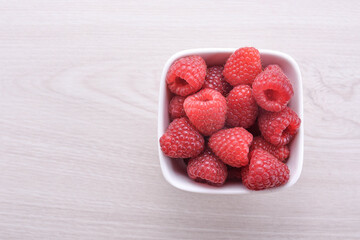 Bowl of fresh raspberries with green leaves on wooden background. Top view