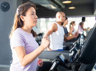 Fototapeta na wymiar Young adult woman doing cardio workout running on treadmill at fitness center