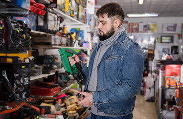 Positive cheerful male is standing with new impact wrench in tools store