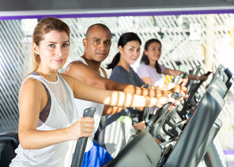 People having running elliptical trainer class in health club