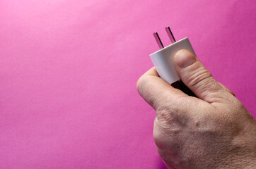 Man's hand holds white DC wall adapter against pink background.