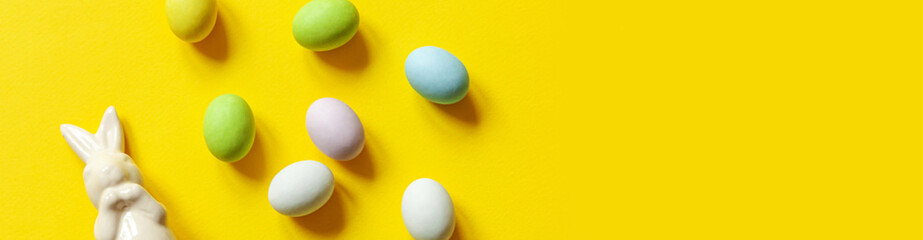 Happy Easter concept. Preparation for holiday. Easter candy chocolate eggs bunny and jellybean sweets isolated on trendy pastel blue background. Simple minimalism flat lay top view copy space. Banner