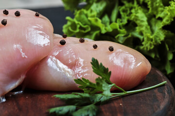 Wooden plate of raw chicken fillet with greens on dark table