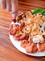 A hand picking on the set of Northen Thai appetizer. The appetizer contain fried porks, crispy porks, northern thai sausages, spicy chilli sauce called Nam Phrik Num and vegetables.