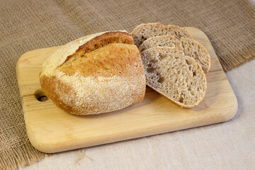 Appetizing freshly baked bread with a golden brown crust on wood cutting board a rough linen cloth close-up