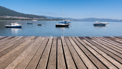 Old wooden footbridge on the seashore with blurred background and boats