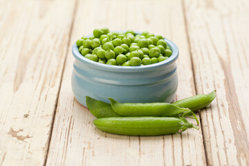 Green peas in blue bowl on white wooden background