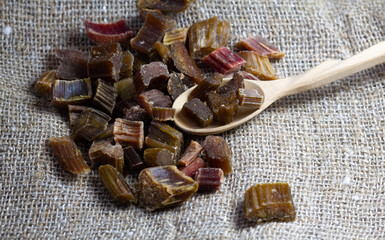 Dried rhubarb candied fruits in a wooden spoon. Candied rhubarb on a canvas fabric background. Dry rhubarb close - up macro photography. Rheum.