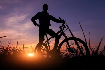 Silhouette of a cyclist against the sunset sky with orange sun and sunlight, copy space