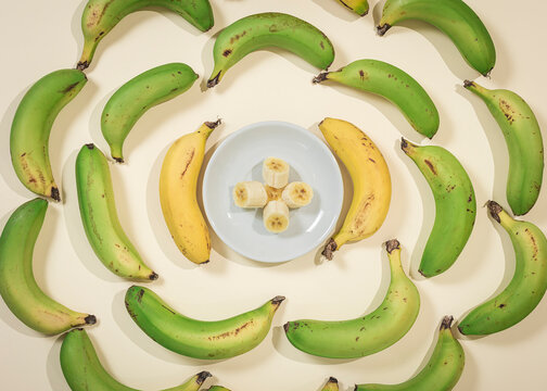 Bananas in a circle with a plate in the center with banana slices.The photo is taken from an overhead point of view and soft colors predominate.
