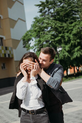 Valentines day celebration, love and dating outdoor concept. Happy loving couple walking on the city street. guess who, young man surprise his girlfriend by putting hands on her eyes