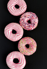 Donuts with pink icing on black background with copy space and flat lay