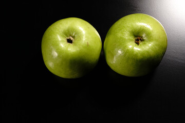 Two green apples on a black background. In the semi-darkness.