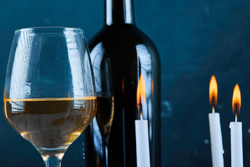 A glass of white wine and bottle on blue background with candles