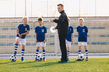Young man soccer coach explaining training rules to group of children. Boys in football team on...