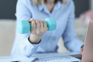 Woman sits on laptop and holds blue dumbbell in her hand