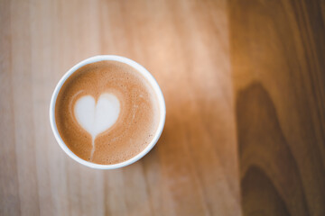 Latte art heart in a paper cup for take away on wooden table. For who love to drink coffee everyday for fresh in the morning. Copy space for text. Top view.