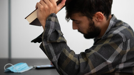 Young man holding a book and touching his head with it
