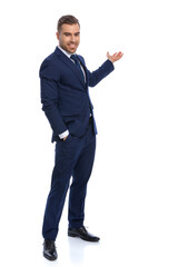 elegant fashion man in navy blue suit presenting to side and smiling