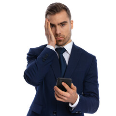upset businessman in suit holding phone and face palming