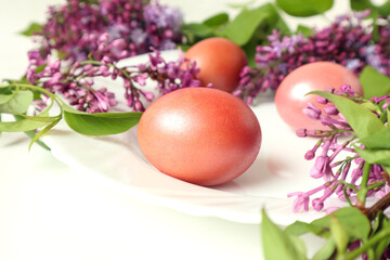 Easter eggs on a white platter with lilac branches, close-up