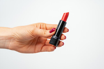 Female hand holding red lipstick against gray background