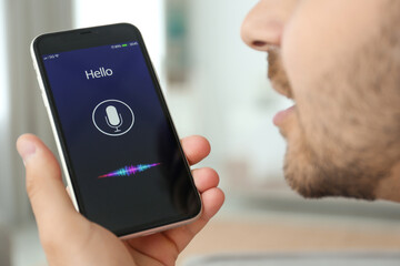 Young man using voice search on smartphone indoors, closeup