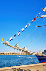 International maritime signal flags on a flagpole on a sailing ship with the harbor in the background.