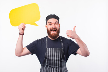 Photo of cheerful chef man showing thumb up and holding empty speech bubble.